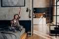 Young beautiful woman sitting on bed stretching with her hand up while holding cup of coffee Royalty Free Stock Photo