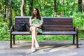 Young lonely woman sitting on bench in park. Shot of a college student enjoying in park outdoors. Teen in pistachio-colored dress Royalty Free Stock Photo