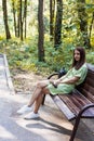 Young beautiful woman sitting on bench in park. Shot of a college student enjoying in park outdoors. Teen in pistachio-colored Royalty Free Stock Photo