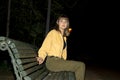 Woman sitting in a bench in a public city park at night while looking to camera