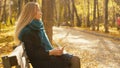 Young beautiful blond woman sitting on bench and uses smartphone in autumnal park. Royalty Free Stock Photo