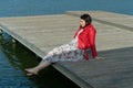 Young beautiful woman sitting on a bridge by the lake, legs down