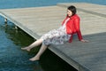 Young beautiful woman sitting on a bridge by the lake, legs down