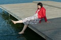 Young beautiful woman sitting on a bridge by the lake, legs down