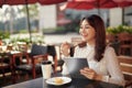 Young beautiful woman sitting in a city center during a sunny day, using a digital tablet pad near a coffee store bar, smiling Royalty Free Stock Photo