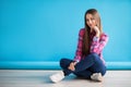 Young beautiful woman sitting on the floor on blue background Royalty Free Stock Photo