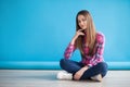 Young beautiful woman sitting on the floor on blue background Royalty Free Stock Photo