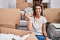 Young beautiful woman sitting on the floor at new home holding money looking positive and happy standing and smiling with a Royalty Free Stock Photo