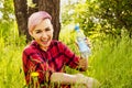 Young beautiful woman sitting in green grass, holds and drink bottle of water on a tree and bush background Royalty Free Stock Photo