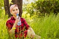 Young beautiful woman sitting in green grass, holds and drink bottle of water on a tree and bush background Royalty Free Stock Photo