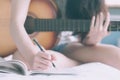 Young beautiful woman sitting on her bed in the bedroom holding guitar composing a song and writing song in textbook ,musician,