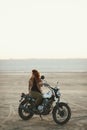 Young beautiful woman sitting on her old cafe racer motorcycle in desert at sunset or sunrise Royalty Free Stock Photo