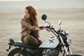 Young beautiful woman sitting on her old cafe racer motorcycle in desert at sunset or sunrise Royalty Free Stock Photo