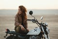 Young beautiful woman sitting on her old cafe racer motorcycle in desert at sunset or sunrise Royalty Free Stock Photo