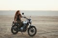 Young beautiful woman sitting on her old cafe racer motorcycle in desert at sunset or sunrise Royalty Free Stock Photo