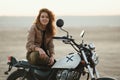 Young beautiful woman sitting on her old cafe racer motorcycle in desert at sunset or sunrise Royalty Free Stock Photo