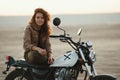 Young beautiful woman sitting on her old cafe racer motorcycle in desert at sunset or sunrise Royalty Free Stock Photo