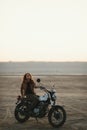 Young beautiful woman sitting on her old cafe racer motorcycle in desert at sunset or sunrise Royalty Free Stock Photo