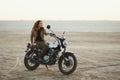 Young beautiful woman sitting on her old cafe racer motorcycle in desert at sunset or sunrise Royalty Free Stock Photo