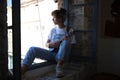 Young and beautiful woman sitting in her studio at work playing the ukulele and looking out of the window while being inspired by