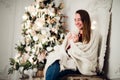 Young beautiful woman with sitting home holding cup of hot coffee wearing knitted warm sweater. Christmas tree Royalty Free Stock Photo