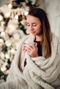 Young beautiful woman with sitting home holding cup of hot coffee wearing knitted warm sweater. Christmas tree Royalty Free Stock Photo