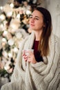 Young beautiful woman with sitting home holding cup of hot coffee wearing knitted warm sweater. Christmas tree Royalty Free Stock Photo
