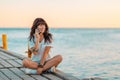 A young beautiful woman is sitting on a pier by the sea and talking on the phone. Sea and sky in the background. Copy space. The Royalty Free Stock Photo