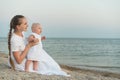 Young beautiful woman sitting on sandy beach and holding baby girl. Mother and child on sea background Royalty Free Stock Photo