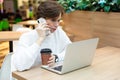 Young beautiful woman sitting at a shopping center at a table and working at a computer laptop, using mobile phone Royalty Free Stock Photo