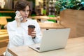 Young beautiful woman sitting at a shopping center at a table and working at a computer laptop, using mobile phone Royalty Free Stock Photo