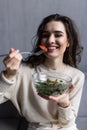 Young and beautiful woman sitting on sofa at home, eating colorful fresh vegetable salad and smiling, healthy woman enjoying food Royalty Free Stock Photo