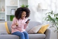 Young beautiful woman sitting on sofa in living room with phone in hands, winner happy with good news received on Royalty Free Stock Photo