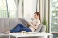 Young beautiful woman sitting on the sofa reading a book enjoying her tea in living room at home Royalty Free Stock Photo