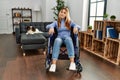 Young beautiful woman sitting on wheelchair at home smiling looking to the side and staring away thinking Royalty Free Stock Photo