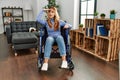 Young beautiful woman sitting on wheelchair at home very happy and smiling looking far away with hand over head Royalty Free Stock Photo