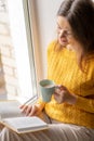 Young beautiful woman near window yellow knitted sweater read book