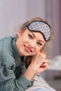 A young beautiful woman in a sleep mask lies on the bed and smiles