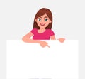 Young beautiful woman smiling and holding a blank / empty sheet of white paper or board and pointing with index finger. Royalty Free Stock Photo