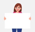 Young beautiful woman smiling and holding a blank / empty sheet of white paper or board. Woman showing a empty poster. Royalty Free Stock Photo