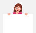 Young beautiful woman smiling and holding a blank / empty sheet of white paper or board. Woman showing a empty poster. Royalty Free Stock Photo