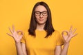 Young beautiful woman smiling and making zen yoga gesture isolated on yellow background Royalty Free Stock Photo