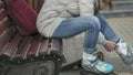 Young beautiful woman in sporty warm clothes and rollers, sitting on a wooden bench and dresses roller skates getting Royalty Free Stock Photo