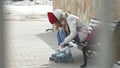 Young beautiful woman in sporty warm clothes and rollers, sitting on a wooden bench and dresses roller skates getting Royalty Free Stock Photo