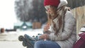 Young beautiful woman in sporty warm clothes and rollers, sitting on a wooden bench and dresses roller skates getting Royalty Free Stock Photo