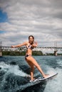 Young beautiful woman stand on surfboard and vigorously rides on wave