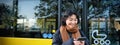 Young beautiful woman standing on bus stop, texting message on smartphone, holding mobile phone, checking her schedule