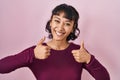 Young beautiful woman standing over pink background success sign doing positive gesture with hand, thumbs up smiling and happy Royalty Free Stock Photo