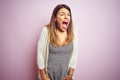 Young beautiful woman standing over pink isolated background angry and mad screaming frustrated and furious, shouting with anger