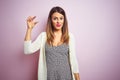 Young beautiful woman standing over pink isolated background smiling and confident gesturing with hand doing small size sign with Royalty Free Stock Photo